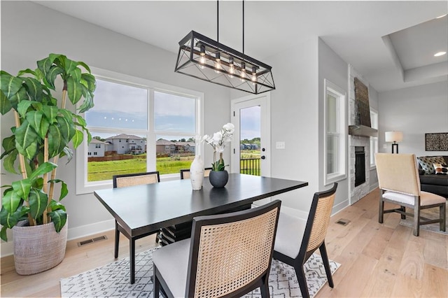 dining room featuring a fireplace, baseboards, visible vents, and light wood-style floors