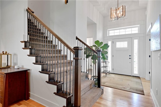 foyer entrance featuring stairs, wood finished floors, a chandelier, a towering ceiling, and baseboards