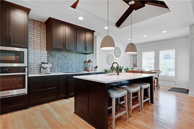 kitchen with stainless steel appliances, light wood-style floors, tasteful backsplash, light countertops, and a center island with sink