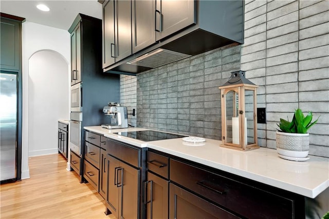 kitchen featuring stainless steel appliances, light wood finished floors, light countertops, decorative backsplash, and arched walkways