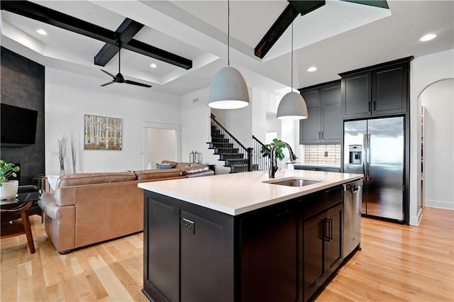 kitchen featuring a sink, stainless steel appliances, light wood-style floors, light countertops, and beam ceiling