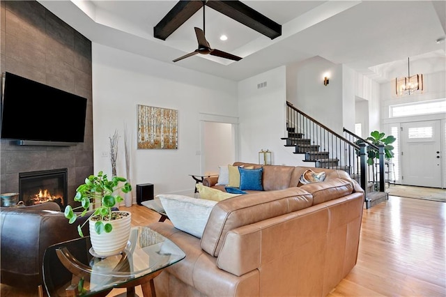 living room with light wood-style flooring, stairs, a tiled fireplace, a high ceiling, and beam ceiling