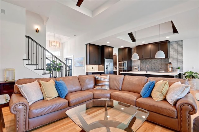 living area featuring a raised ceiling, light wood-style flooring, a chandelier, stairway, and recessed lighting