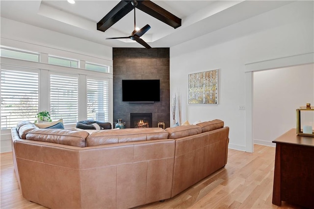 living area with light wood finished floors, ceiling fan, a fireplace, beamed ceiling, and baseboards