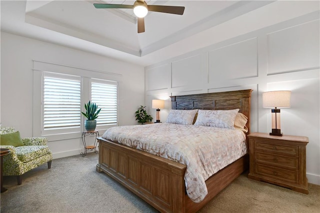 bedroom with light colored carpet, a tray ceiling, baseboards, and a ceiling fan