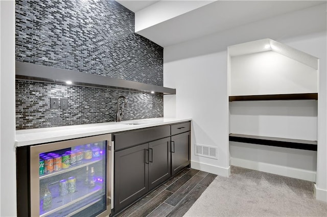 indoor wet bar featuring wine cooler, decorative backsplash, wood tiled floors, and baseboards