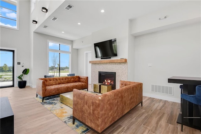 living area featuring a glass covered fireplace, healthy amount of natural light, light wood-type flooring, baseboards, and a towering ceiling