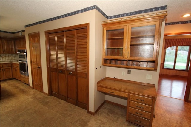 6726 Mill Creek Rd, Shawnee, KS 66217 - kitchen with double oven, a textured ceiling, backsplash, glass insert cabinets, and baseboards