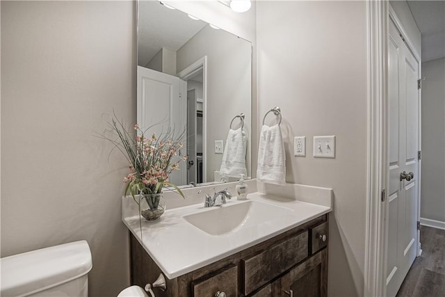 bathroom featuring toilet, baseboards, wood finished floors, and vanity
