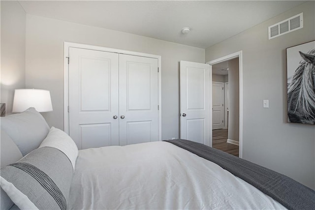 bedroom with baseboards, a closet, wood finished floors, and visible vents