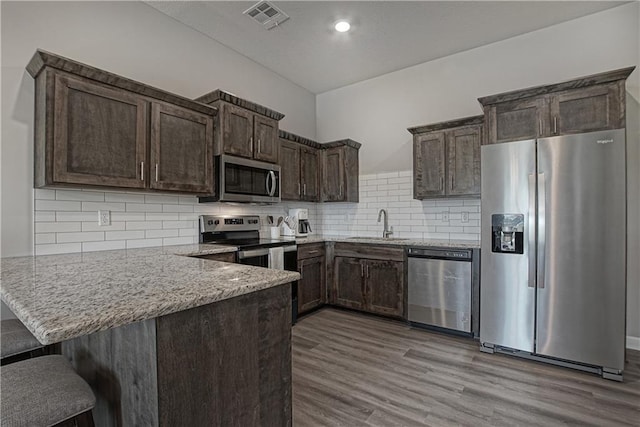 kitchen featuring visible vents, dark brown cabinets, a sink, a peninsula, and stainless steel appliances