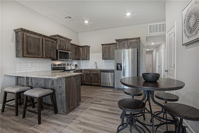 kitchen featuring visible vents, a peninsula, dark brown cabinetry, light wood finished floors, and appliances with stainless steel finishes