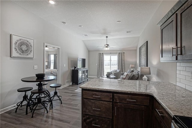 kitchen featuring visible vents, a peninsula, wood finished floors, dark brown cabinetry, and a ceiling fan
