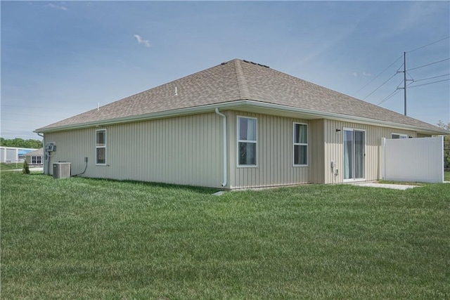 rear view of property with central air condition unit, a shingled roof, and a lawn