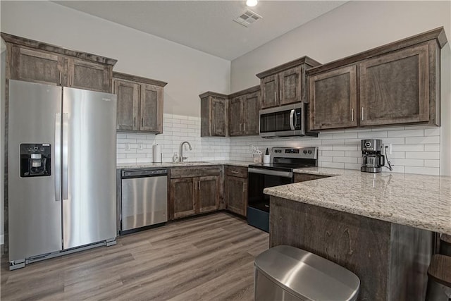 kitchen featuring visible vents, dark brown cabinets, light stone counters, a peninsula, and stainless steel appliances