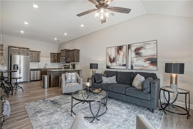 living area with a ceiling fan, baseboards, lofted ceiling, and light wood-type flooring