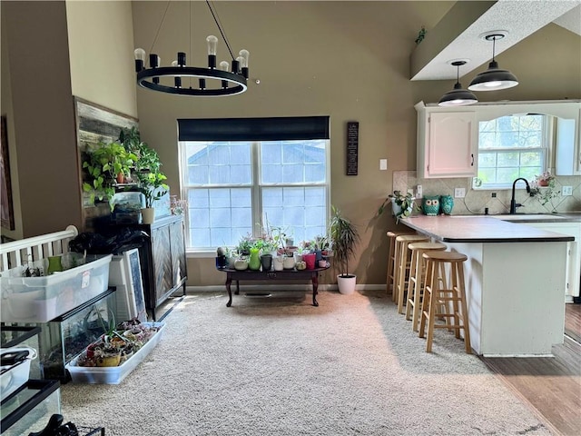 kitchen featuring a kitchen breakfast bar, white cabinetry, a sink, backsplash, and hanging light fixtures