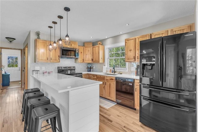 kitchen featuring light wood-style flooring, a sink, a kitchen bar, a peninsula, and black appliances