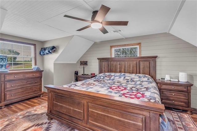bedroom with multiple windows, wooden walls, and wood finished floors