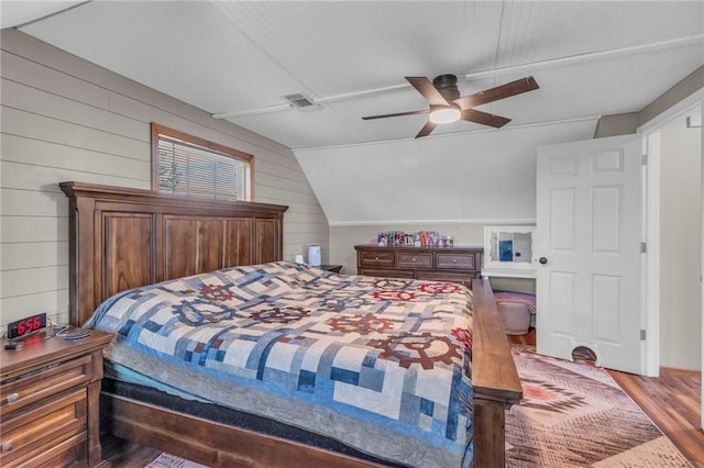 bedroom with ceiling fan, visible vents, wooden walls, vaulted ceiling, and wood finished floors