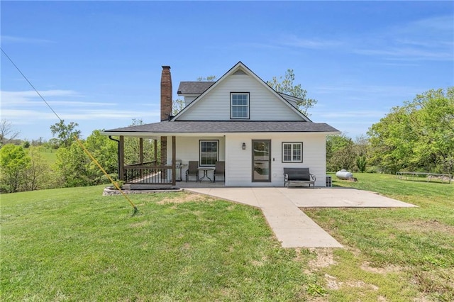 back of house featuring a yard, a patio area, a shingled roof, and a chimney