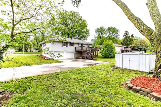 view of yard with an attached garage, a shed, a deck, stairway, and concrete driveway