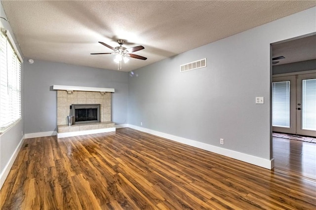 unfurnished living room with visible vents, wood finished floors, baseboards, a tiled fireplace, and a ceiling fan