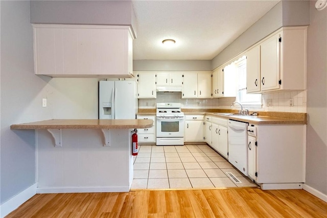 kitchen featuring a sink, baseboards, a peninsula, under cabinet range hood, and white appliances