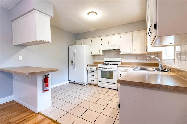 kitchen with white appliances, baseboards, under cabinet range hood, white cabinets, and a sink