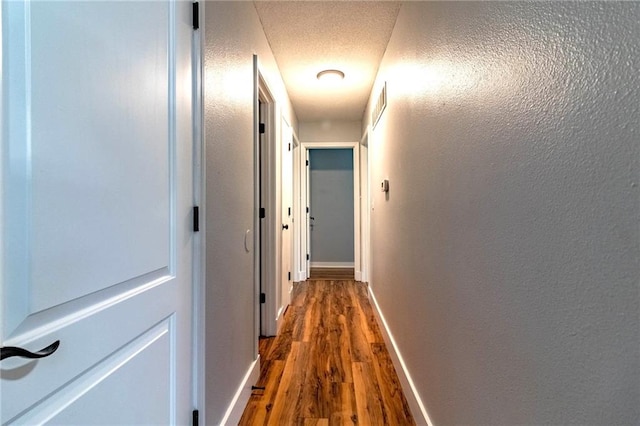 corridor with baseboards, dark wood finished floors, a textured wall, and visible vents