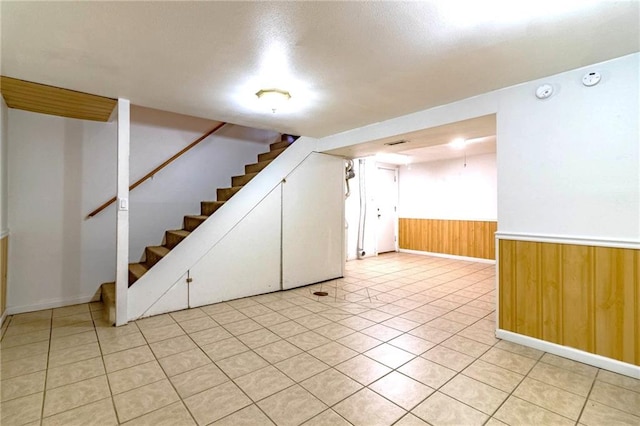 spare room with baseboards, wooden walls, stairway, a wainscoted wall, and light tile patterned floors