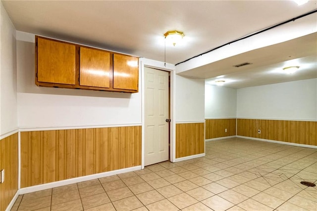 empty room featuring wood walls, visible vents, and a wainscoted wall