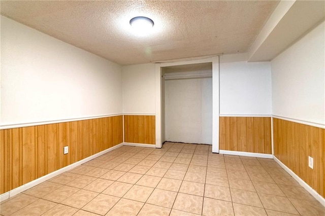unfurnished bedroom featuring wooden walls, a closet, a textured ceiling, and a wainscoted wall