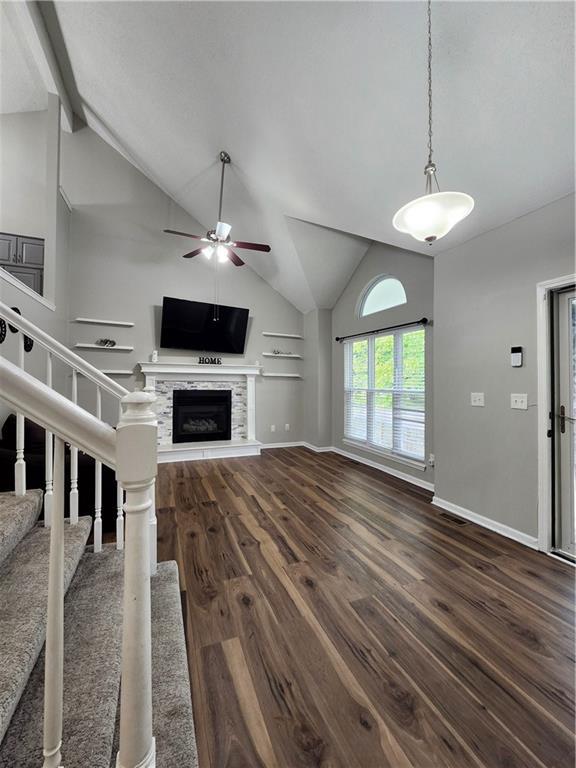 unfurnished living room with ceiling fan, stairway, a fireplace with raised hearth, dark wood-style floors, and vaulted ceiling with beams