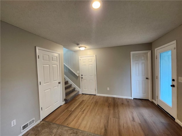 below grade area featuring visible vents, stairs, wood finished floors, baseboards, and a textured ceiling