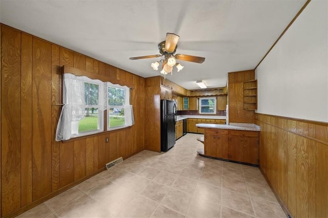 26335 W 321st Ter, Paola, KS 66071 - kitchen featuring freestanding refrigerator, brown cabinetry, wood walls, a peninsula, and a ceiling fan