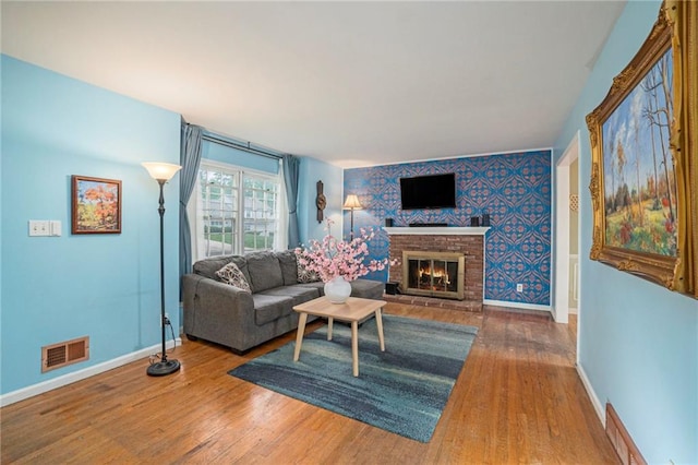 living room featuring a brick fireplace, baseboards, visible vents, and wood finished floors