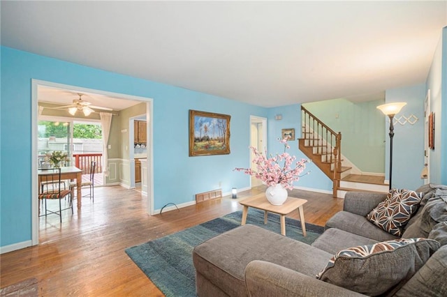 living room with visible vents, wood finished floors, baseboards, stairway, and a ceiling fan