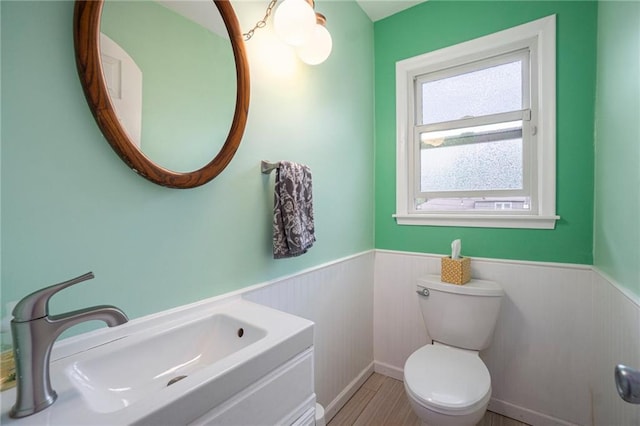 bathroom with wood finished floors, a sink, a wainscoted wall, and toilet