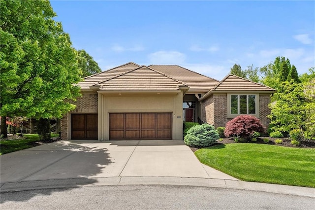 view of front of property with an attached garage, concrete driveway, a front yard, a tile roof, and brick siding