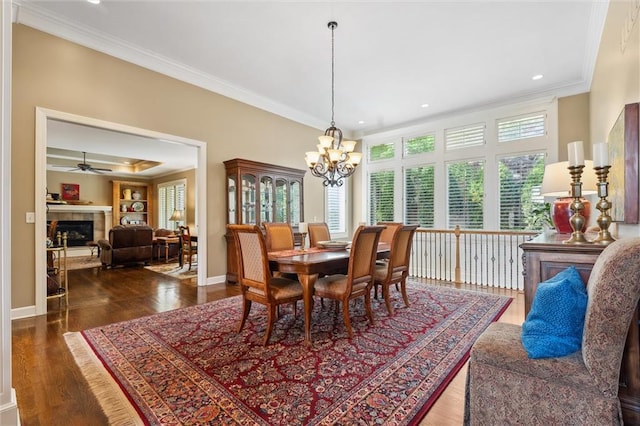 dining room with crown molding, a tiled fireplace, wood finished floors, a chandelier, and baseboards