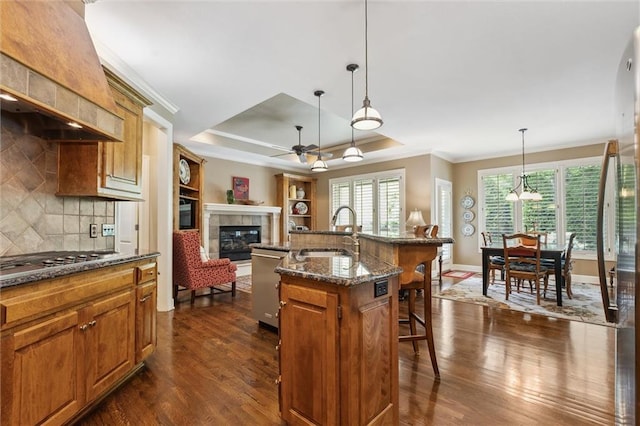 kitchen with a sink, crown molding, a kitchen bar, a tiled fireplace, and dark wood-type flooring
