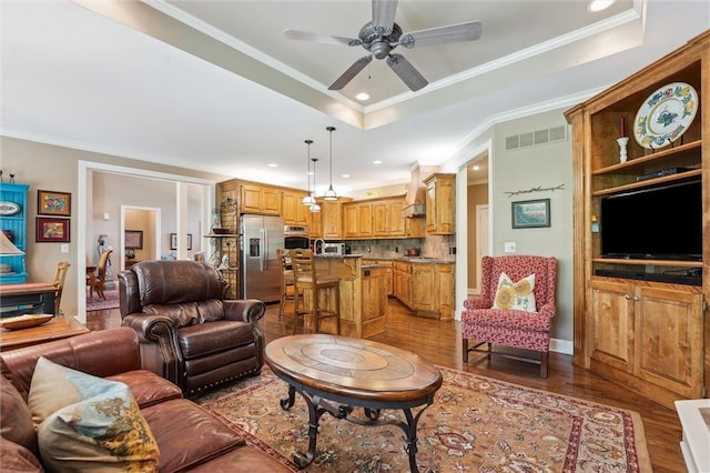 living area with wood finished floors, ceiling fan, ornamental molding, recessed lighting, and a raised ceiling