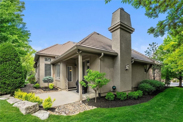 rear view of property with stucco siding, a chimney, a tiled roof, a lawn, and a patio area