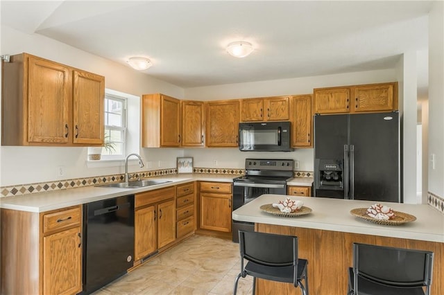 kitchen with black appliances, a sink, light countertops, a breakfast bar, and a peninsula