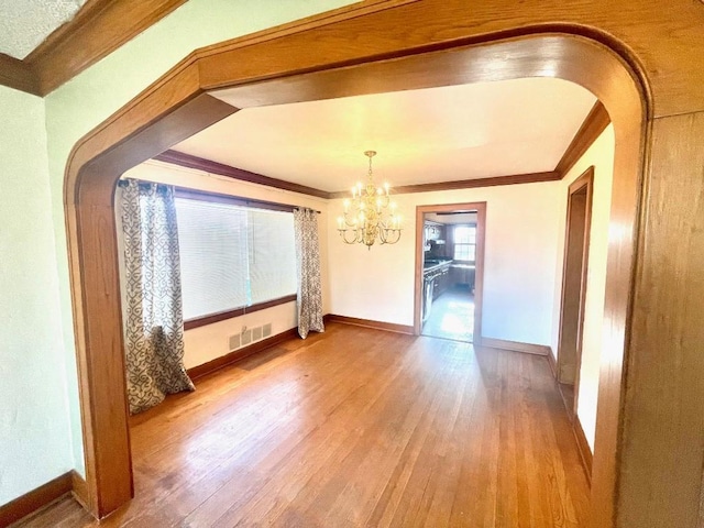 unfurnished dining area featuring visible vents, wood finished floors, ornamental molding, and arched walkways
