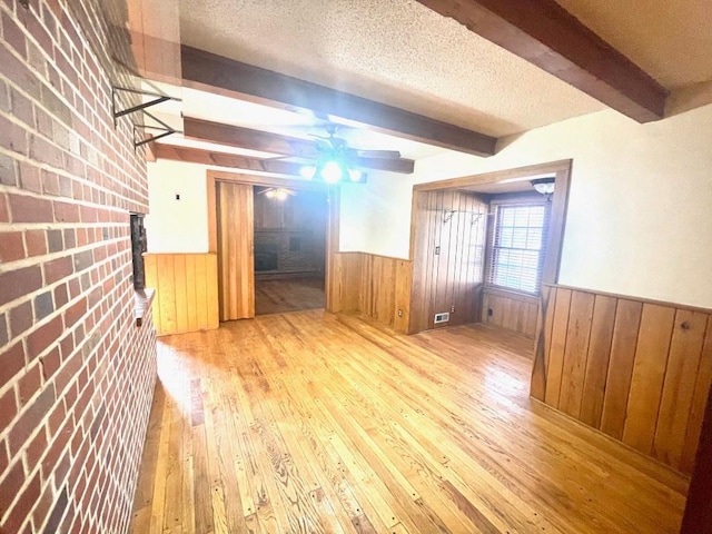 spare room featuring a wainscoted wall, a textured ceiling, hardwood / wood-style floors, and beamed ceiling