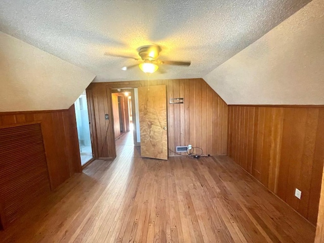 additional living space with a textured ceiling, wooden walls, and light wood-style floors