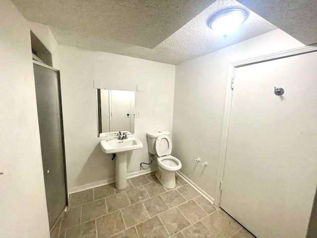 bathroom featuring a shower stall, a textured ceiling, toilet, and baseboards