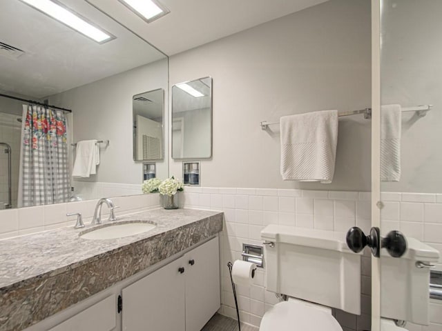 bathroom with tile walls, toilet, a shower with shower curtain, a wainscoted wall, and vanity